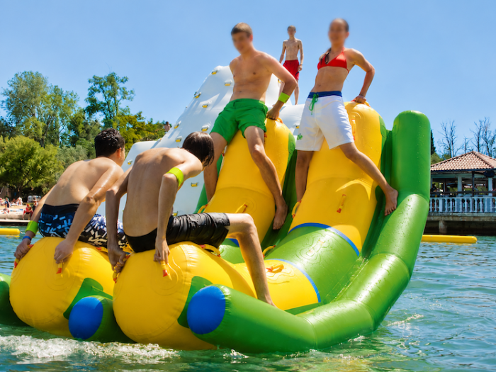 Group balancing on green and yellow inflatable double rocker toy on a lake
