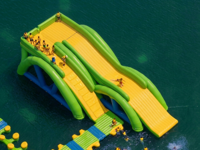 Aerial view of green and yellow floating water slide with riders on a lake water park