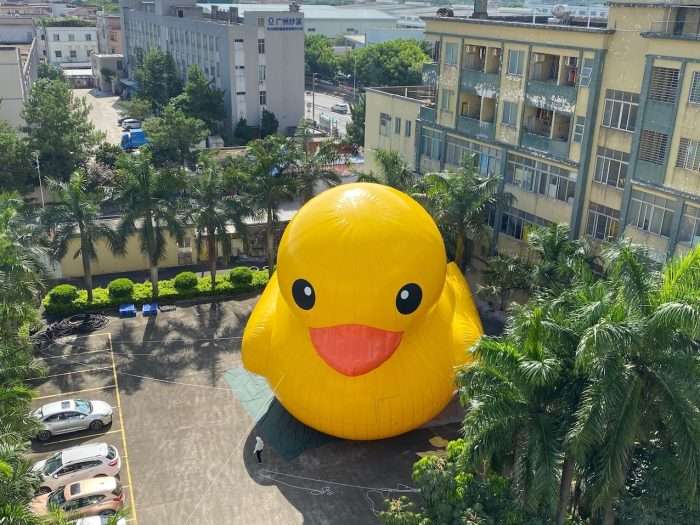 Aerial view of giant inflatable PVC tarpaulin yellow rubber duck installed in a parking lot surrounded by palm trees and buildings