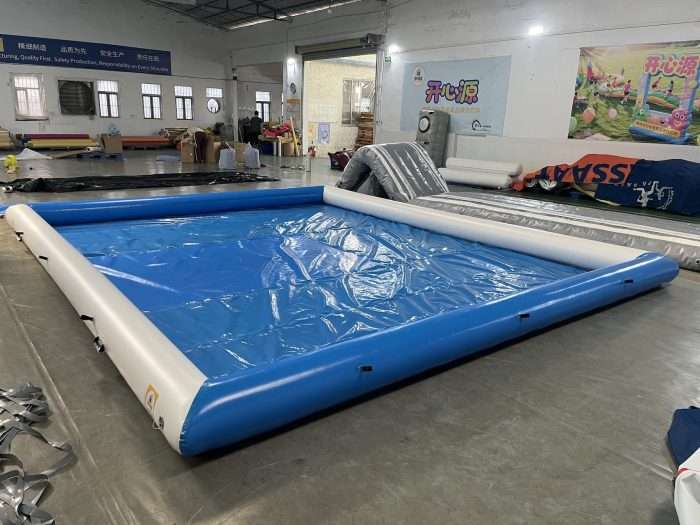 Blue and white inflatable pool with attached gray entry ramp slide in warehouse