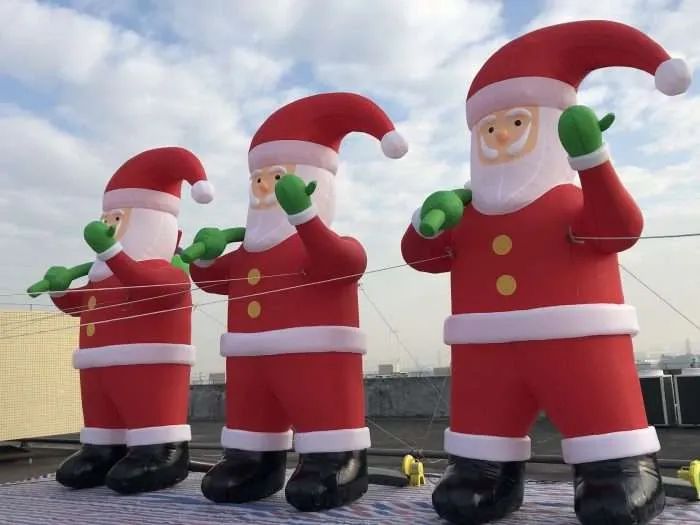 Low angle view of giant inflatable Santa Claus figures waving against blue sky, 5m