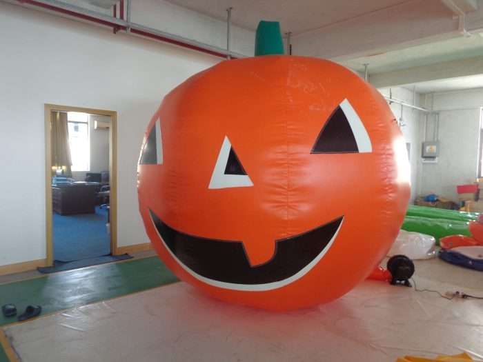 Giant inflatable pumpkin with jack-o'-lantern face and a small air blower unit connected at its base
